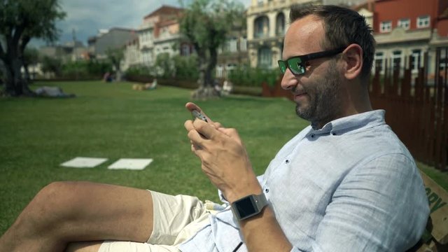 Happy man playing game on smartphone sitting in garden in cafe

