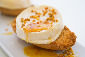  Goat cheese with honey and pollen on white plate, macro, isolated