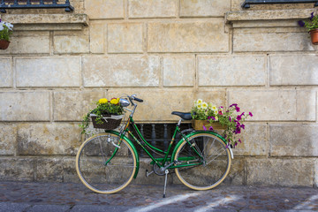 Fototapeta na wymiar Green bicycle with flowers on the basket leaning on a wall