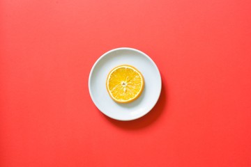 Orange slice on white plate with red colored background