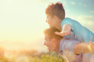 Happy father and son having fun over beautiful sky outdoors. Summer holidays, vacation