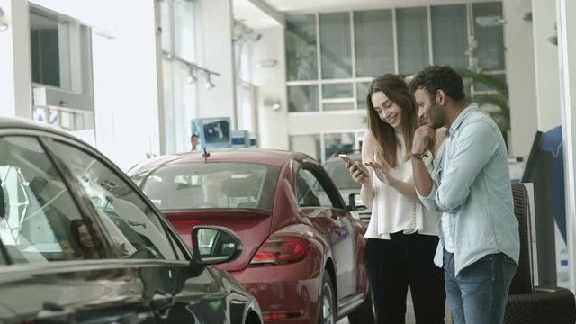 Swarht guy and beautiful girl uses the smartphone in car showroom