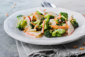 Vegetable salad with broccoli,apple,carrots, pine nuts and sauce in white plate on light stone table background. Healthy vegetarian food/ Copy space
