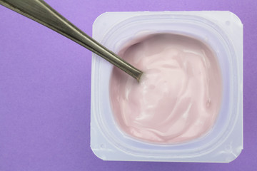 Healthy strawberry fruit flavored yogurt with natural coloring in plastic cup isolated on purple background with small silver spoon - top view