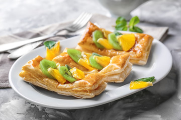 Plate with delicious puff pastries and fruits on grey table