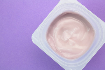 Fototapeta na wymiar Healthy strawberry fruit flavored yogurt with natural coloring in plastic cup isolated on purple background - top view shot in studio