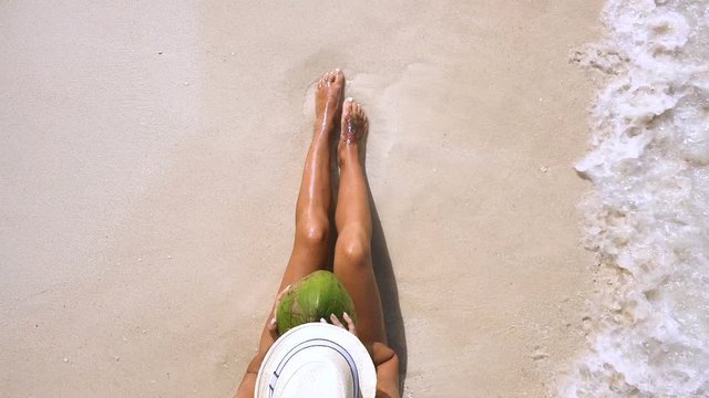Sexy girl in a hat holds a pineapple on the beach with waves
