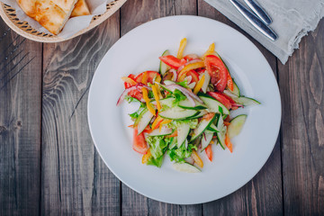 Vegetable salad with tomato, cucumber, pepper onion and lettuce in white plate on wooden table background. Healthy vegetarian food content
