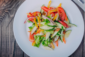 Vegetable salad with tomato, cucumber, pepper onion and lettuce in white plate on wooden table background. Healthy vegetarian food content