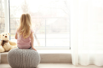 Small girl sitting on ottoman near window