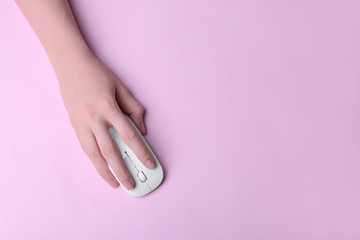 Female hand holding computer mouse on pink background