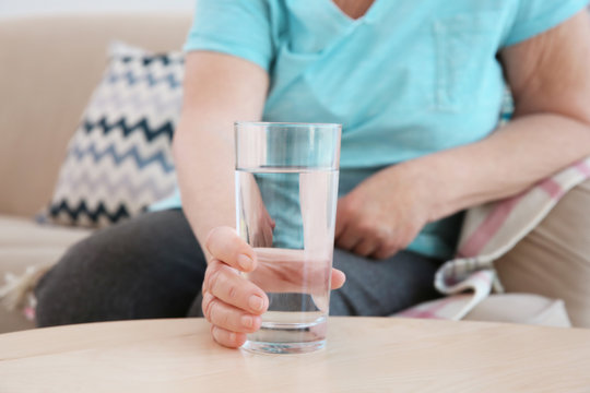 Elderly woman holding glass of water on table. Concept of retirement