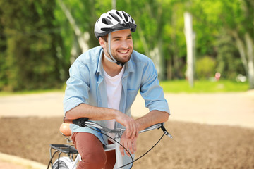 Handsome young man with bicycle and helmet in park on sunny day