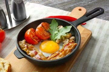 Frying pan with tasty egg, bacon and tomatoes on table