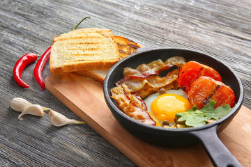 Frying pan with tasty egg, bacon and tomatoes on table