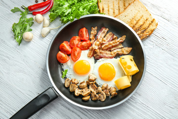 Frying pan with tasty eggs, bacon and mushrooms on table