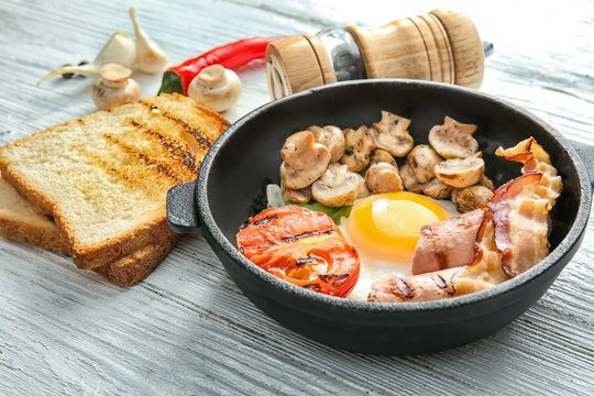 Frying pan with tasty egg, bacon and mushrooms on table