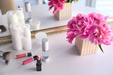 Beautiful bouquet with fragrant peonies and cosmetics on dressing table near mirror