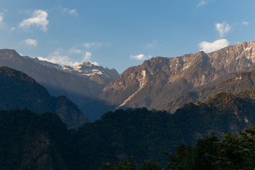 Green hill near Kangchenjunga mountain with clouds above and trees with sunlight that view in the evening in North Sikkim, India.