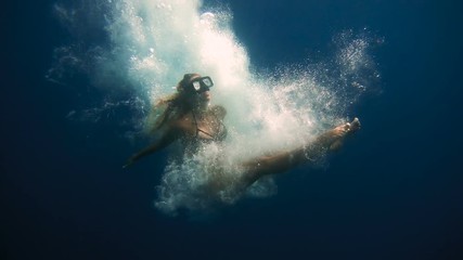 Young and beautiful girl is ducking under the water and beautifully falls to the bottom among the bubbles and boats on the background