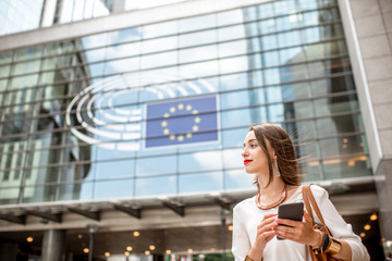Young businesswoman standing with phone near the Parliament building of European Union in Brussel...