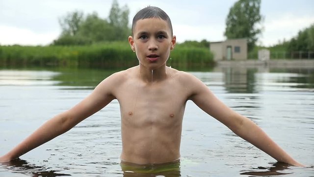 Wonderful view on a young boy who keeps hands aside and touches water, while standing in a lake. He smiles and dives impressively in slow motion. The bushes of reed are seen in the background