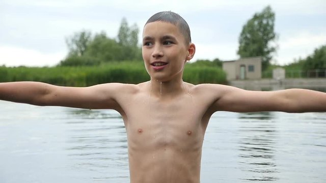 Original view on a young boy who keeps hands aside while standing in a lake. He smiles and falls in water impressively  in slow motion. The bushes of reed are seen in the background.