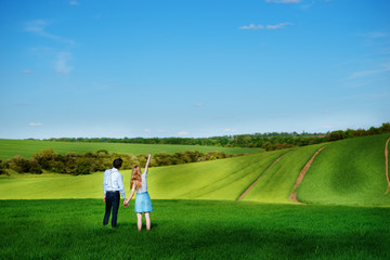 A young couple standing in the field, the girl shows her hand to the sky
