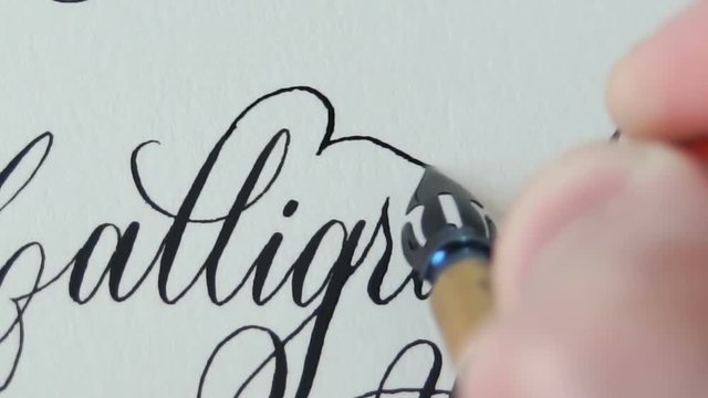 Calligrapher writing a word Calligraphy with point nib pen and black ink on white paper.