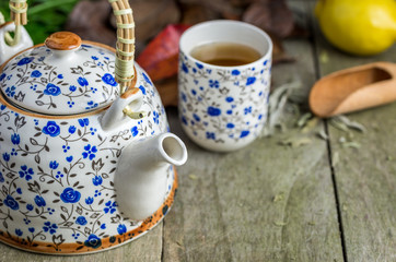 Glass of tea with tea pot and lemon on natural wooden table.