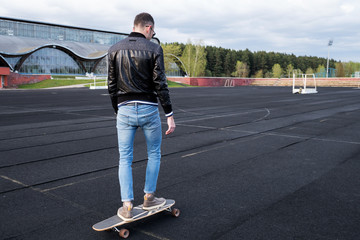 Man riding a skateboard on a sportsground, view from the back