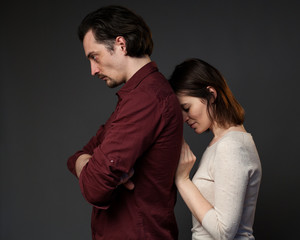Family quarrel, woman is touching the back of her husband, gray background