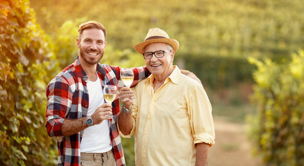 smiling father and son tasting wine in vineyard.
