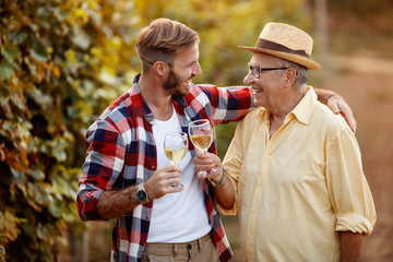 Father and son tasting wine in vineyard.