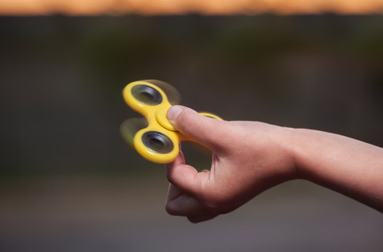 Little girl is playing a yellow spinner in her hand outdoors.