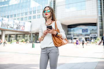 Fototapeta premium Young businesswoman standing with phone near the Parliament building of European Union in Brussel city