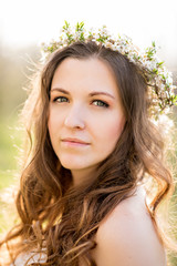 Beautiful young girl in white dress and wreath of flowers on head in blooming gardens