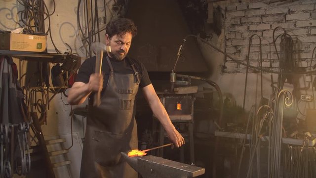Blacksmith works with metal on anvil in forge