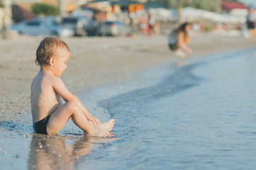 the child is seated near the sea, in the water, washes the feet of
