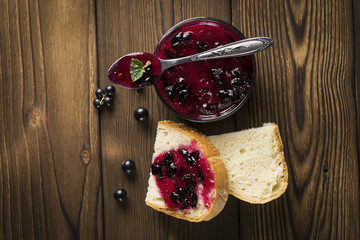 black currant jam with bread on wood background