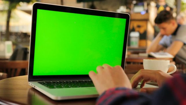 Woman using laptop computer with green screen while sitting outside in the cafe. Female hands typing on laptop keyboard. Close up. Chroma key