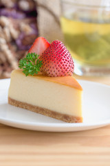 Homemade New York cheesecake on white plate decorated by strawberry and parsley. Moist and smooth classic style baked cheesecake. Copy space background of delicious strawberry New York cheesecake.
