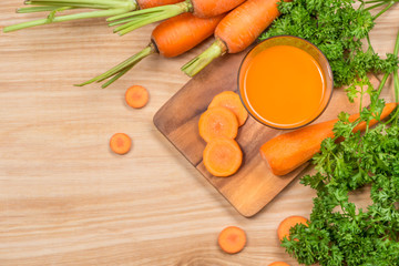 Glass of fresh carrot juice with vegetables on wooden table.