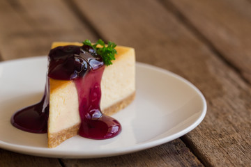 Homemade blueberry cheesecake on white plate decorated with parsley and blueberry sauce. Moist and smooth classic baked cheesecake. Copy space background of delicious blueberry New York cheesecake.