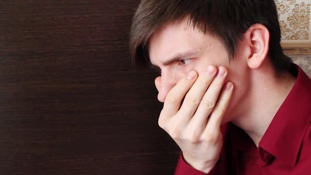 A young guy in a red shirt covered his mouth with his hand, looks closely