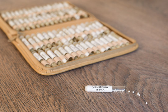Globuli Causticum und im Hintergrund eine Taschenapotheke mit Globuli