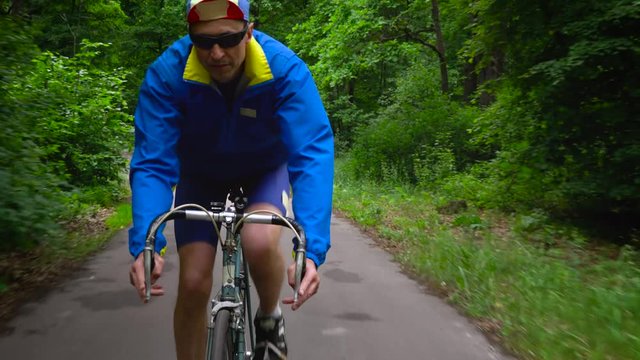 Middle-aged man is riding a road bike along a forest road
