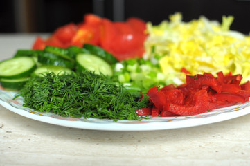 Fresh organic sliced vegetables on the white plate on the wooden table. Close up, selective focus.