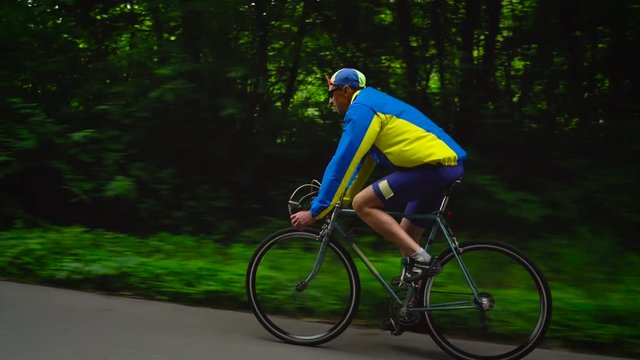 Middle-aged man is riding a road bike along a forest road