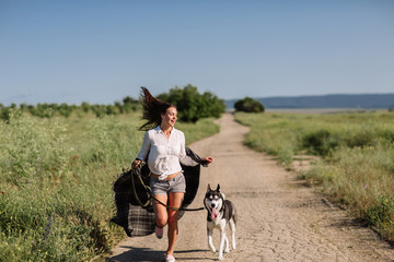 Fototapeta premium Beautiful girl plays with a dog (black and white husky with blue eyes) green field